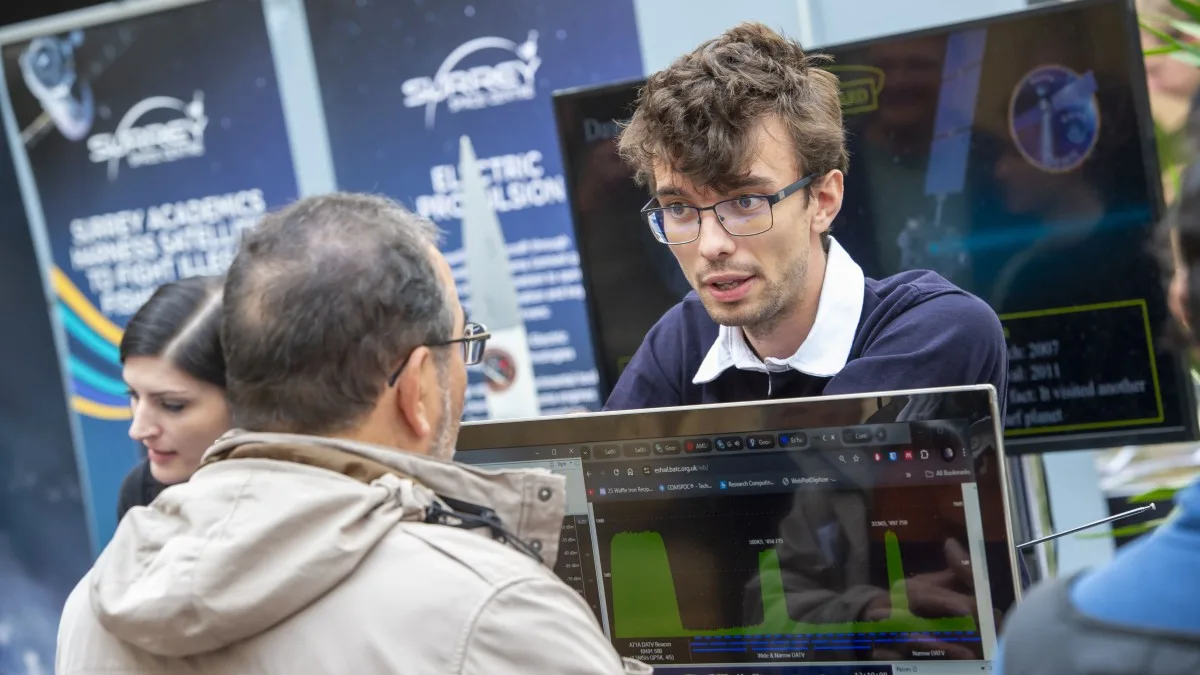 A Surrey Space Centre researcher explains satellite signal data on a laptop to a visitor at a stand with Surrey Space Centre banners about electric propulsion