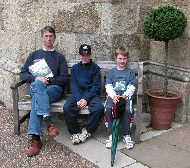 John Murphy and two boys sitting on a wooden bench by a stone wall